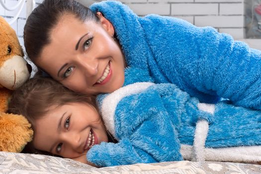 Happy mother and daughter in blue terry robes on the bed