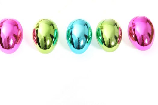 Line of vibrant shiny Easter Eggs in pink, green abd blue on a white background with copyspace for your seasonal greeting