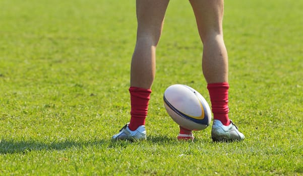 A rugby player's legs preparing to kick a rugby ball.