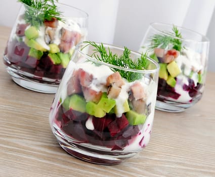 Beetroot salad with avocado and herring in cream sauce in a glass