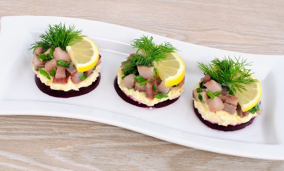 Appetizer of herring with onions on the beets and eggs, lemon and dill