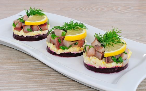 Appetizer of herring with onions on the beets and eggs, lemon and dill