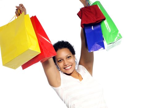 Beautiful rejoicing African American woman with her shopping raising handfuls of colourful carrier bags in the air showing off her purchases isolated on white