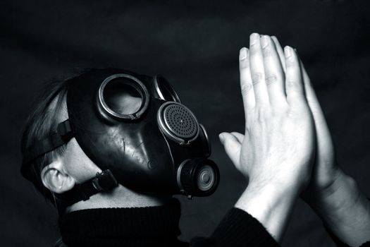 The man in a gas mask on a dark background. Hands are combined as at prayer