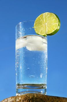 Cold glass of water with ice against a blue sky