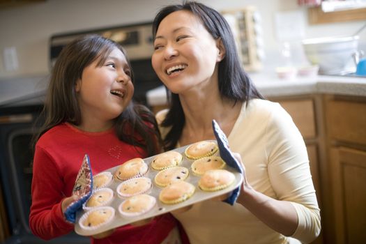 Asian mother and daughter baking muffins in the kitchen at home