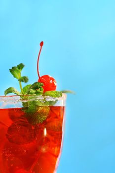 Red tropical drink with mint and cherries against a blue sky