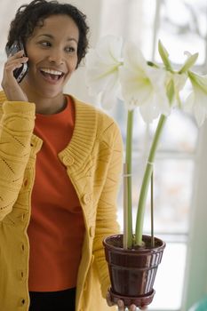 Smiling beautiful African American woman talking on a cell phone holding a flowering plant