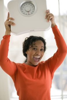 Beautiful African American woman holding scale over her head cheering her success