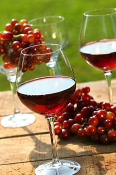 Three glasses of red wine with grapes on rustic table