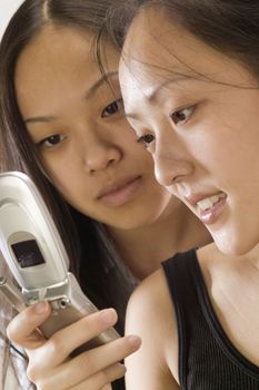 Two young Asian woman looking at the display of a cell phone