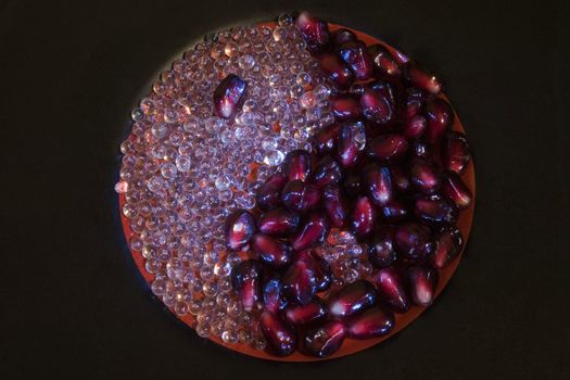 Yin-Yang sign made from glass beads and pomegranate arils on black plate