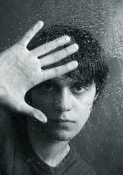 The young man behind wet glass
