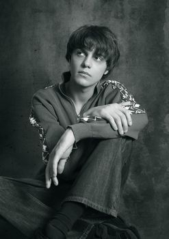 Portrait of the young in studio. Hands are crossed in a lap. b/w+blue tone