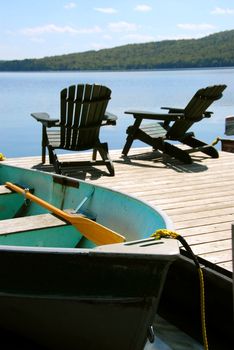 Paddle boat and two adirondack wooden chairs on dock facing a blue lake