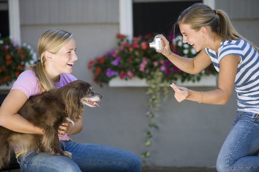 Teen girl poses with her dog while best friend takes photo with digital camera