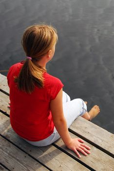 Young girl dipping feet in the lake from a wooden boat dock