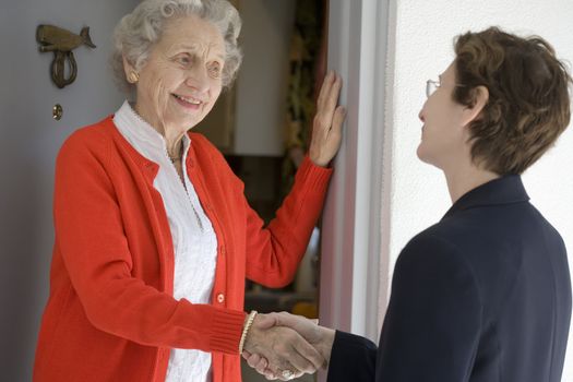 Attractive senior woman shaking hands with visitor at her front door