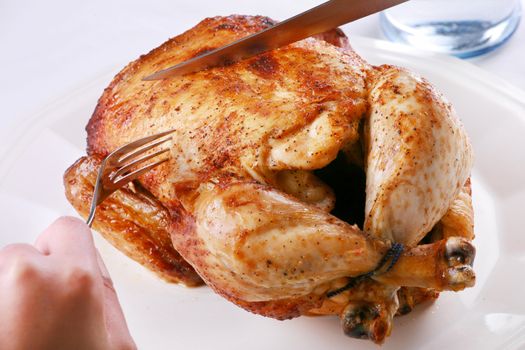 Hands carving rotisserie chicken with fork and knife
