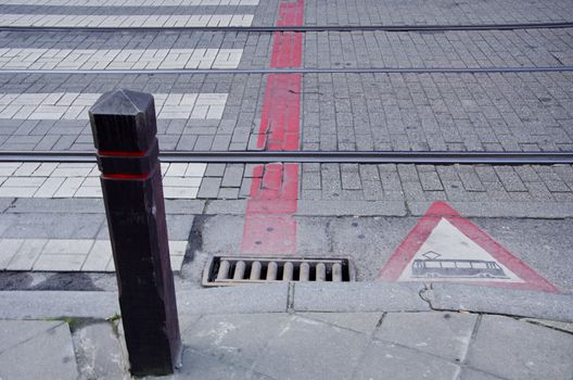 Sidewalk and tram rails. Warning sign. Fragment of street. Passenger transportation.