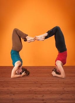 Two women perform Vrisikasana yoga posture on a wooden mat