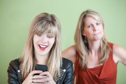 Angry woman behind excited teen on mobile phone