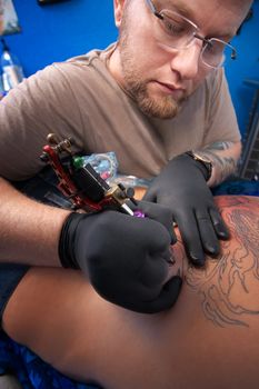 Caucasian Tattoo technician engraves a tattoo on woman's back