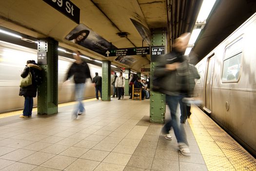 Commuter passengers waiting and walking in subway trainstation platform while train carts are arriving during rush hour. MTA in New York City at 59th Street and Lexington Avenue.