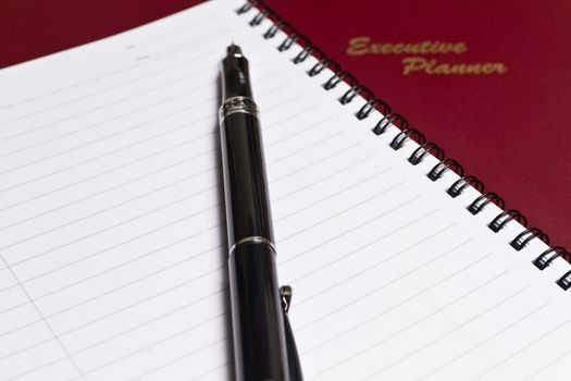 a brown executive planner with spiral note book and a pen in lanscape orientation