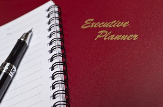 angled view of a  marron executive planner with spiral note book and a pen in lanscape orientation