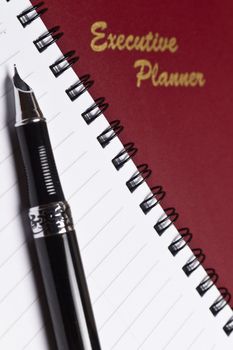angled view of a marroon executive planner with spiral note book and a pen in portrait orientation