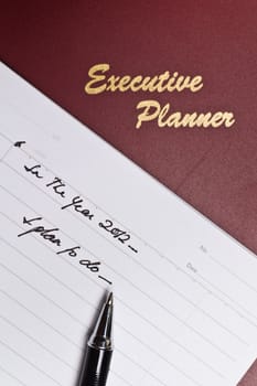 angled view of a  dark red executive planner with spiral note book and a pen in portrait orientation