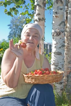 Senior woman holds in flat basket with a ripe berries and big strawberry