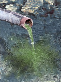 Green contaminated water poring out from pipe into fresh drinking water.