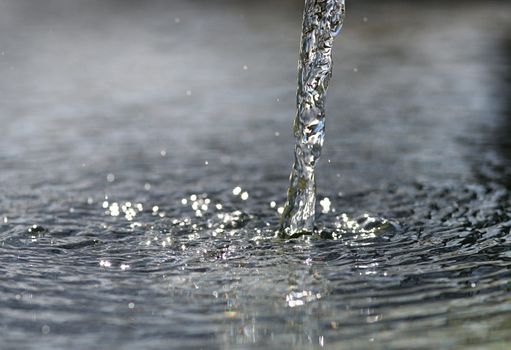 Highly detailed fresh and clear water beam pouring down into water surface.