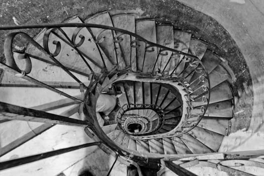 Looking down an old winding spiral stairs with a metal rail