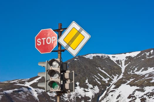 Stop! Road signs and traffic light on blue sky and mountains