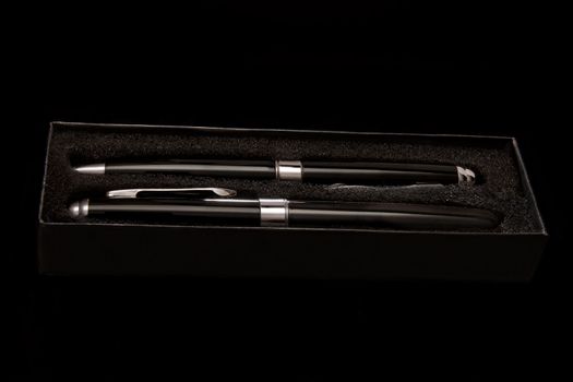 Two black pens in a black case on a black background