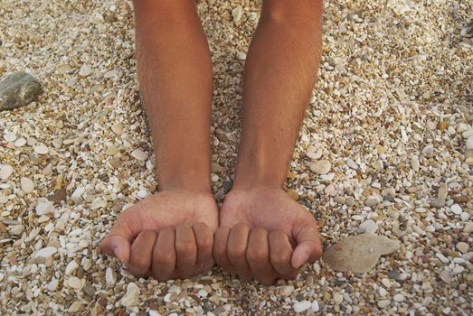 Man tanned hands compressed into cams against background of small stones on the beach