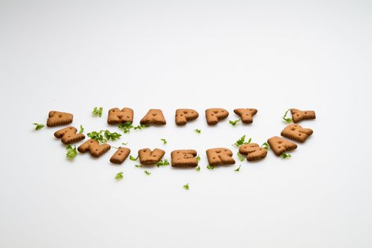 Angled view of the Happy anniversary wording by brown biscuits and green leaves on white surface