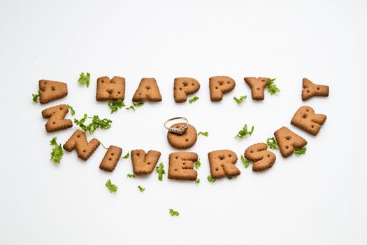 Happy anniversary wording by brown biscuits, ring and green leaves on white surface