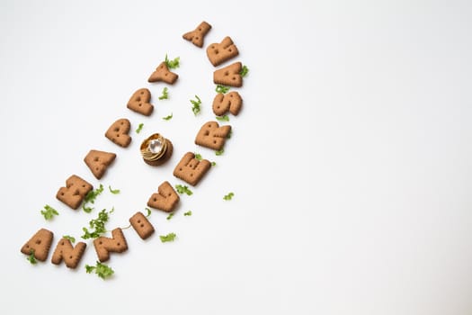 Happy anniversary wording by brown biscuits, diamond ring and green leaves on white surface slanting position