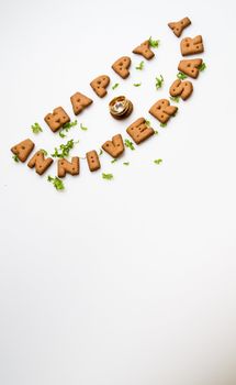 Happy anniversary wording by brown biscuits, diamond ring and green leaves on white surface slanting position