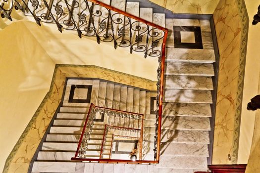 Looking down a winding marble staircase with a metal rail