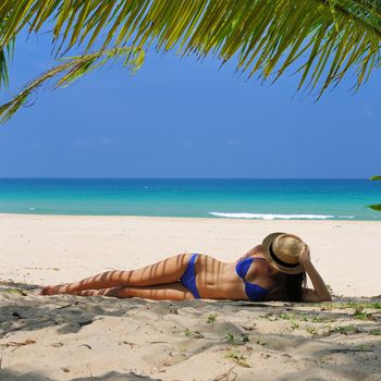 Woman at beach under palm tree with leaf shadow on her body