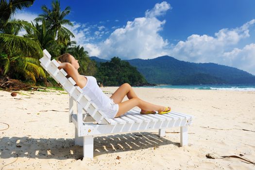 Girl on a tropical beach sitting at chaise lounge