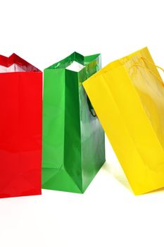 Bright colourful paper shopping bags suitable for recycling in vibrant red, green and yellow standing upright close together on a white background