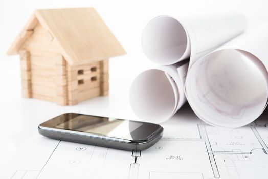 wooden house and smartphone on blueprints