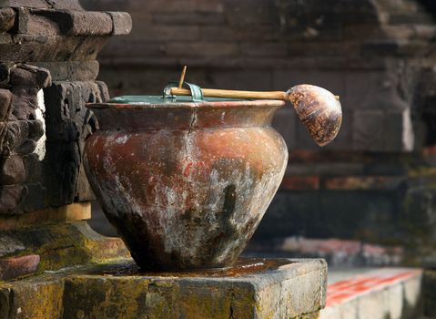 Ancient pot with a ladle before a temple for washing legs. Indonesia. Bali
