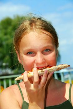 Young girl eating a slice of cheese pizza outside